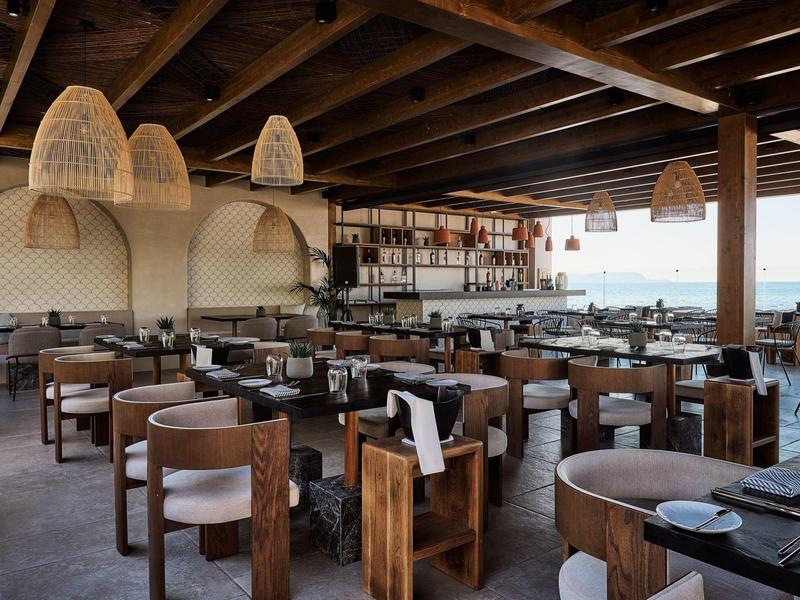 Restaurante moderno con muebles de madera y vista al mar bajo un techo de madera.
