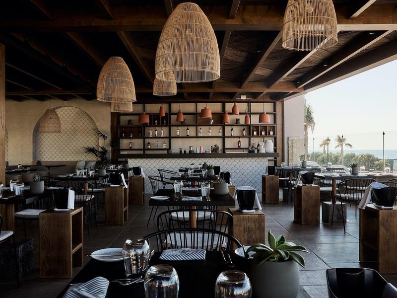 Restaurante moderno con muebles de madera y lámparas de bambú, vista al mar.