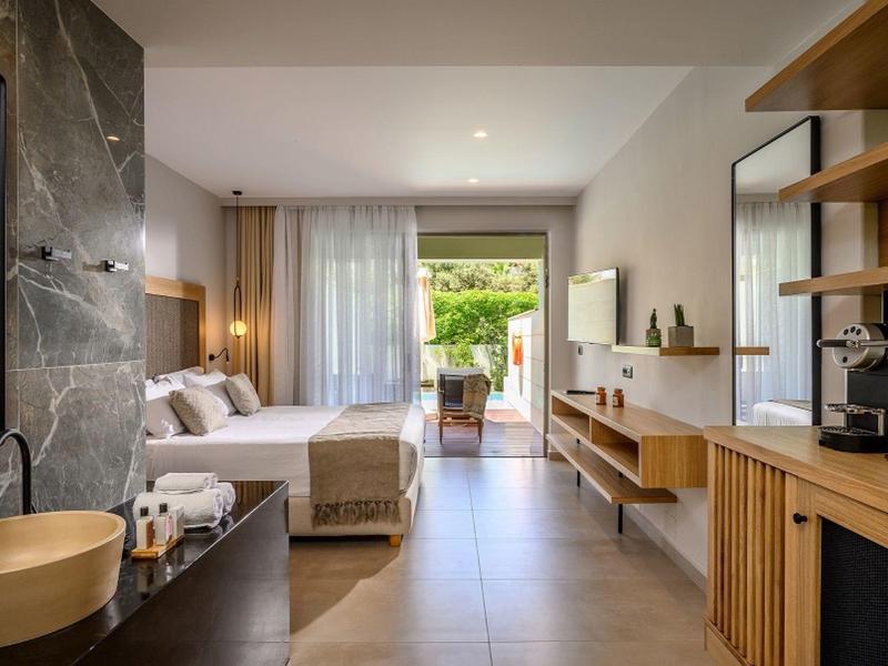 Habitación de hotel moderna con cama doble, baño abierto y terraza con vista al jardín.