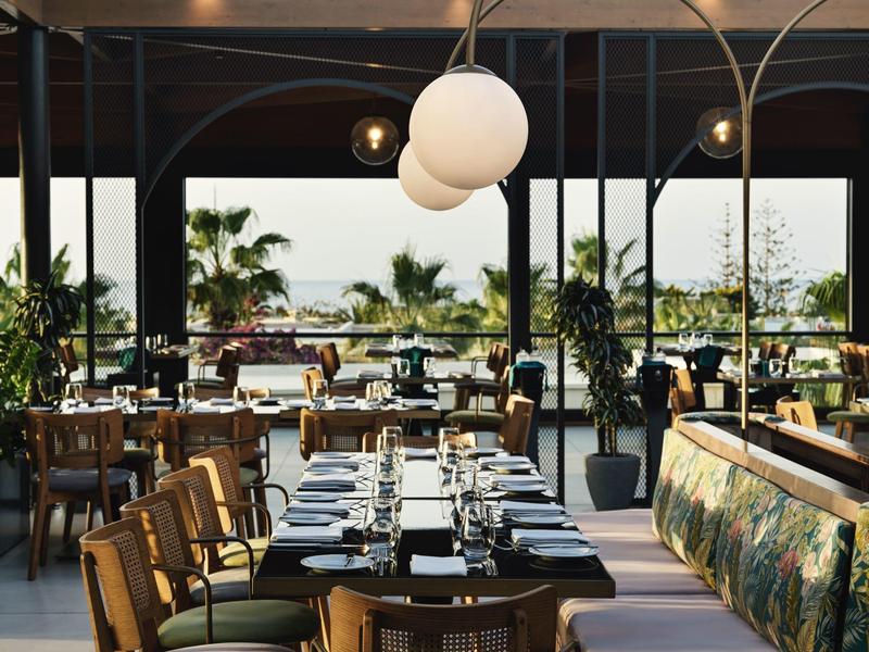 Restaurante moderno con mesas preparadas y vista a palmeras afuera