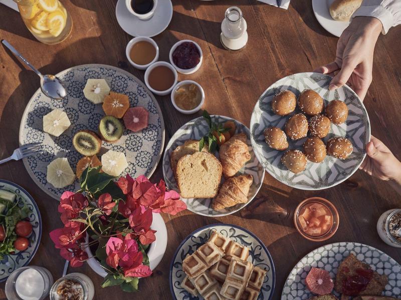 Diversos platos de desayuno sobre una mesa de madera con manos pasando cuencos.