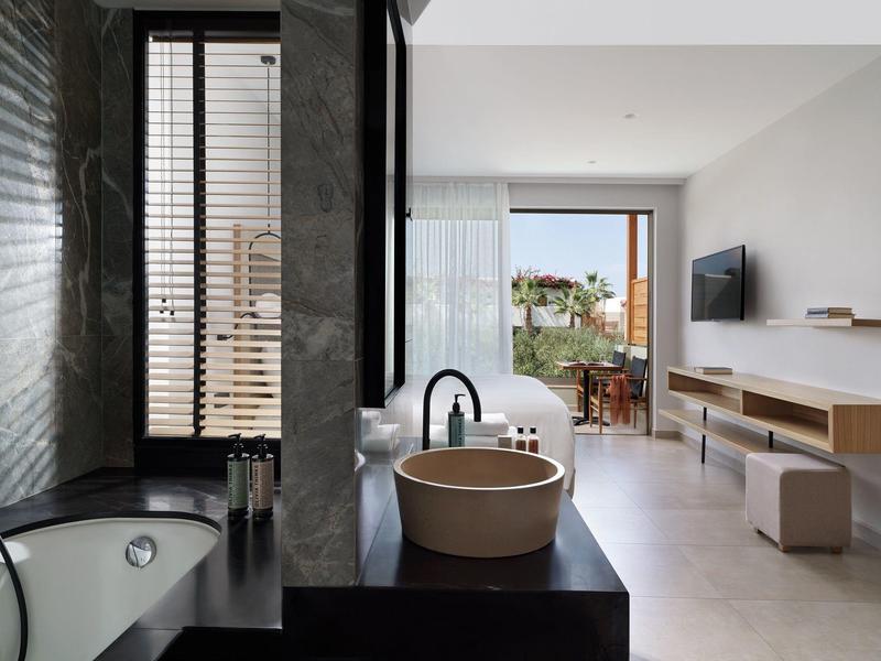 Baño moderno con bañera independiente y lavabo junto a una ventana con vista al salón.