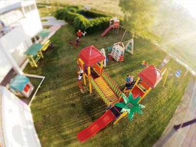Spielplatz mit bunten Klettergerüsten, Rutschen und Schaukeln auf grünem Rasen bei Sonnenschein.