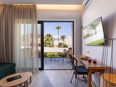 Nowoczesny pokój hotelowy z tarasem, stołem, krzesłami i widokiem na palmy na zewnątrz.