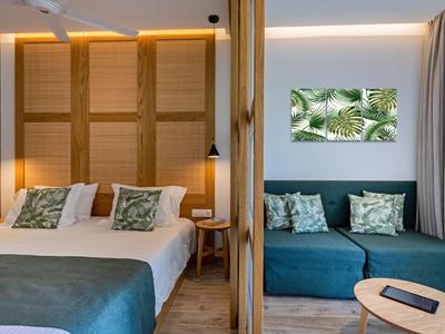 Nowoczesny pokój hotelowy z podwójnym łóżkiem, sofą i tropikalną dekoracją ścienną