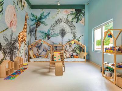 Kinderspielzimmer mit Dschungel-Wandmalerei, Holzspielzeug und großen Fenstern, viel natürlichem Licht.
