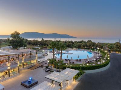 Moderner Hotelpool mit runden Formen, Palmen und Blick auf Meer und Berge bei Sonnenuntergang.