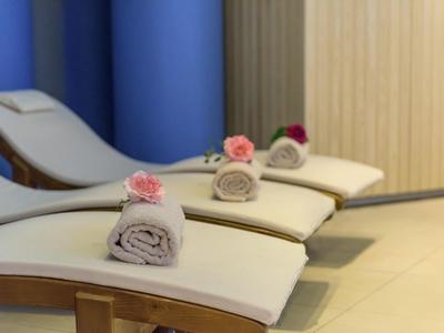 Drei weiße Liegen mit eingerollten Handtüchern und rosa Blumen in einem hellen Raum.