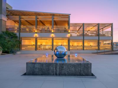 Modernes Gebäude mit gläserner Fassade, beleuchtet bei Sonnenuntergang, davor ein reflektierender Edelstahlball.