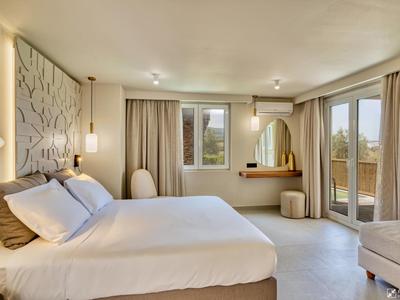 Helles Schlafzimmer mit großem Bett, weichen Vorhängen, Spiegel und Balkon mit Ausblick.