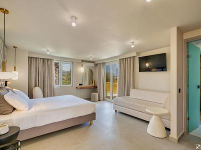 Hell eingerichtetes Schlafzimmer mit Doppelbett, Sofa, großem Fenster und Fernseher an der Wand.
