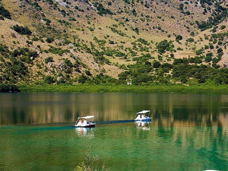 Two small boats sail on a clear green mountain lake with forested slopes.