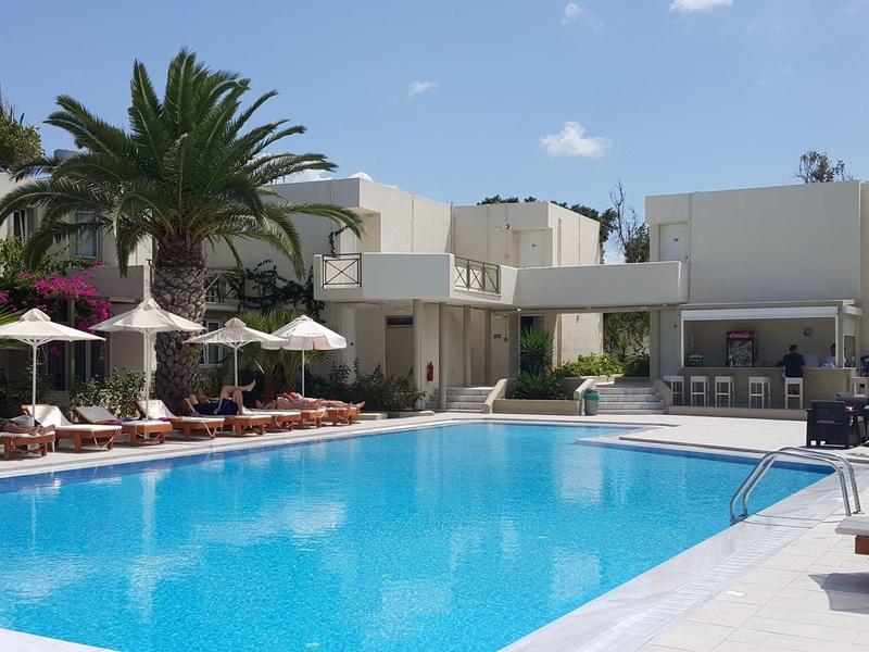 Modern hotel pool with lounge chairs, umbrellas, and palm trees under a blue sky.