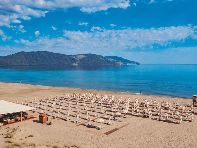 Beach with white umbrellas, calm sea, and mountains in the background.