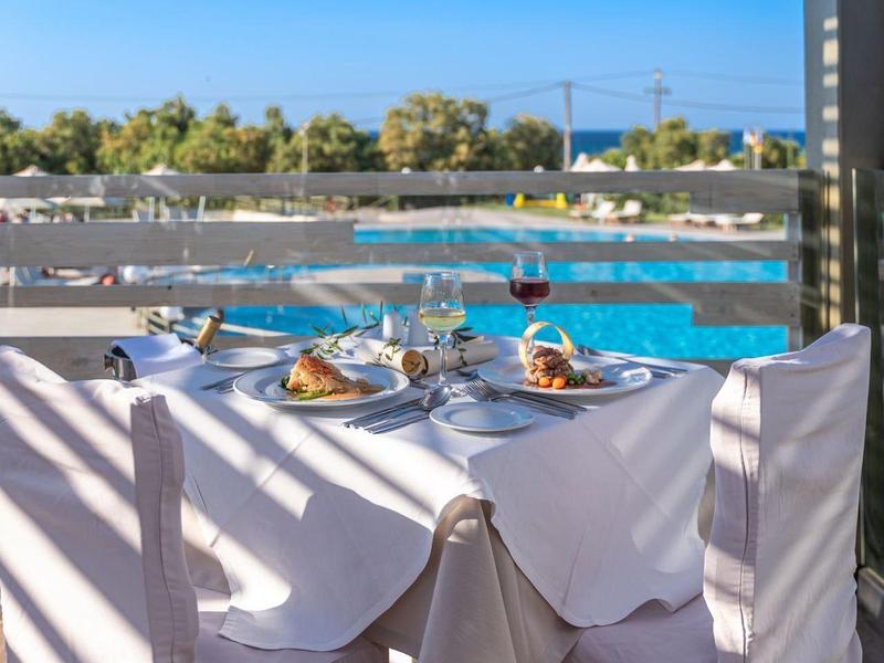 A set dining table with white chairs by the pool under a sunny sky.