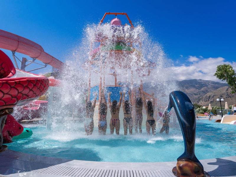 Water park with people under a large water bucket dumping water under a bright sky.