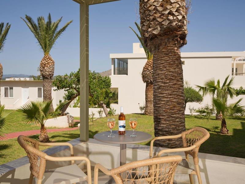 Terrace with glass table, chairs, and palm trees in front of a white building under clear sky.
