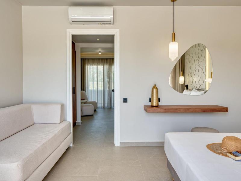 Minimalist hotel room with white furnishings, mirror, and hanging lamp.