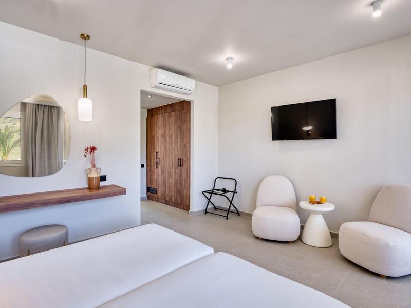 Bright hotel room with cozy chairs, TV, window, and modern decor.