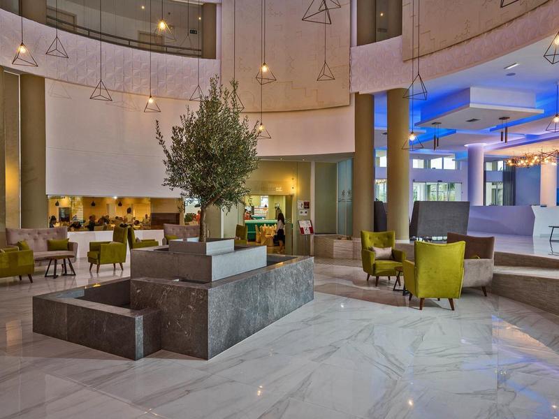 Spacious hotel lobby with marble floor, seating areas, and central plant feature.