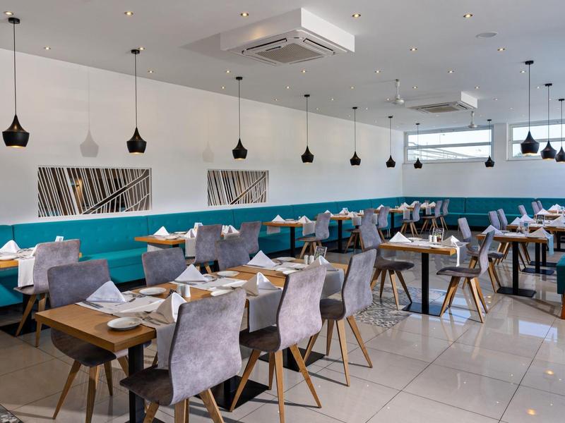 Modern restaurant with blue benches, gray chairs, set tables, and pendant lights.