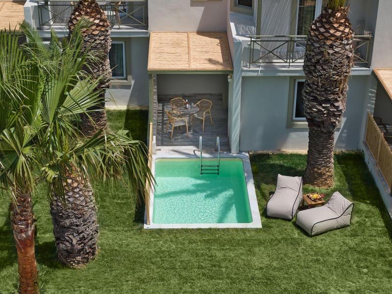 Small pool with lounge chairs on grassy area beside palm trees and house.