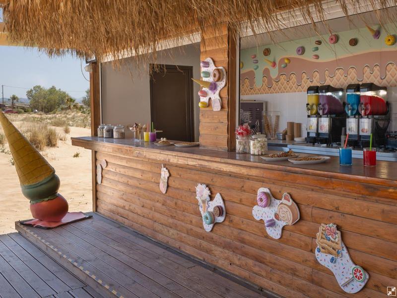 Wooden beach bar with thatched roof and large ice cream cone sculpture next to it.