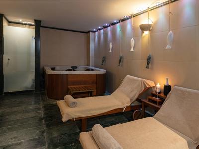 Gemütlicher Wellnessraum mit Whirlpool, zwei Liegen, Handtüchern und stimmungsvoller Beleuchtung.
