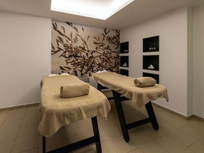Zwei Massageliegen mit braunen Bezügen stehen in einem hellen Raum mit Pflanzenwanddekor.