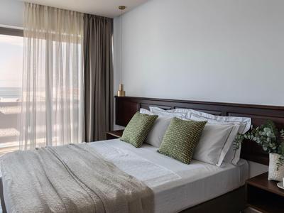Modernes Schlafzimmer mit großem Bett, grauem Überwurf, grünen Kissen und Balkon vor Vorhängen.