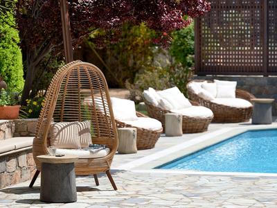 Comode sedie in vimini e una poltrona accanto a una piscina in un giardino soleggiato.