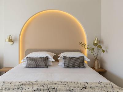 Camera d'hotel moderna con letto matrimoniale, due cuscini, illuminazione soffusa e decorata con piante.