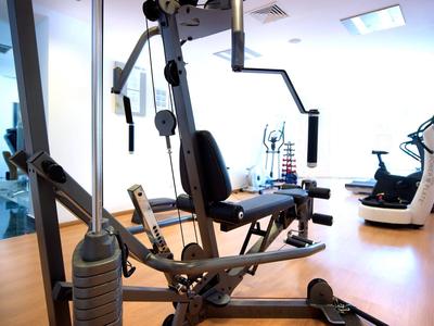 Innenansicht eines modernen Fitnessraums mit Kraftstation, Laufband und hellem Holzboden.