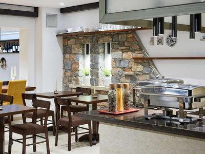 Moderner Speiseraum mit Holztischen, Stühlen, Steinmauer und Buffetstation mit warmhaltenden Behältern.