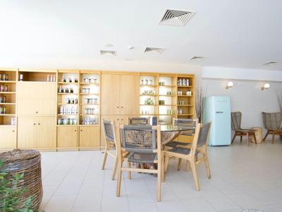 Heller Raum mit Holzmöbeln, Gläsern und Geschirr, mittig runder Tisch und Stühle, im Hintergrund Kühlschrank.
