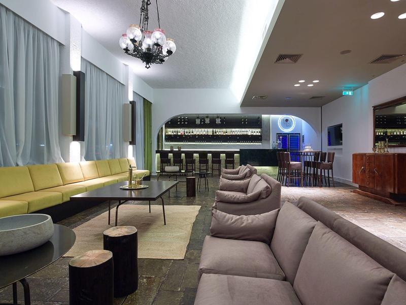 Nowoczesny salon hotelowy z sofami, stolikami i barem w tle.