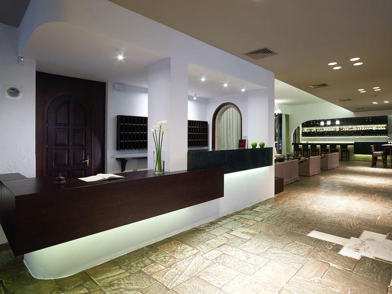 Nowoczesna recepcja hotelowa z ciemnym kontuarem i jasną kamienną podłogą.