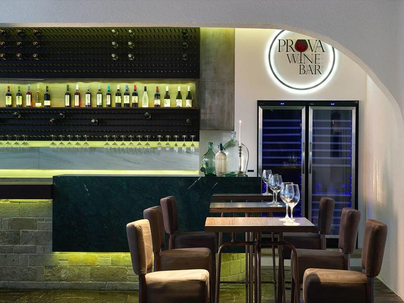 Hotelowy bar z drewnianymi stolikami, tapicerowanymi krzesłami i nastrojowym oświetleniem.