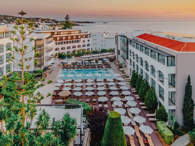 Hotel z rozległym tarasem, stołami i krzesłami, widok na morze o zachodzie słońca.