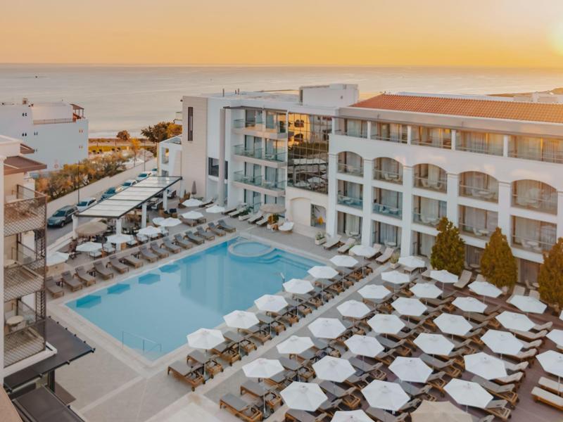 Nowoczesny hotel z zewnętrznym basenem, leżakami i parasolami o zachodzie słońca.