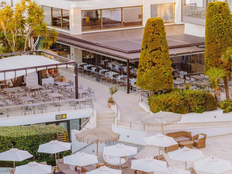 Nowoczesny taras hotelowy z stołami, krzesłami i dużymi białymi parasolami.