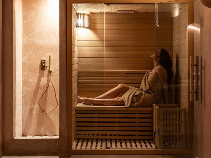 Kobieta relaksująca się w drewnianej saunie, ciepła atmosfera i przytłumione światło.