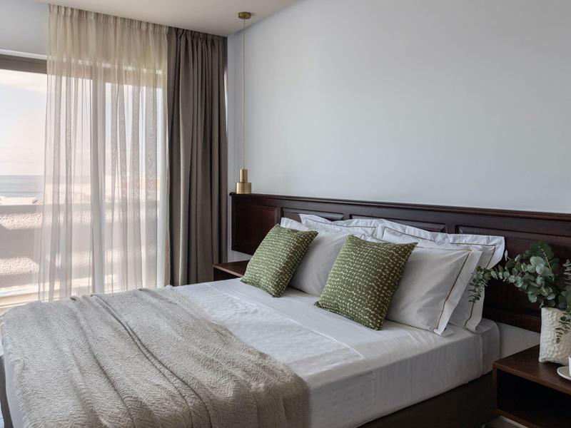 Nowoczesny pokój hotelowy z podwójnym łóżkiem, zielonymi poduszkami i dużym oknem na balkon.