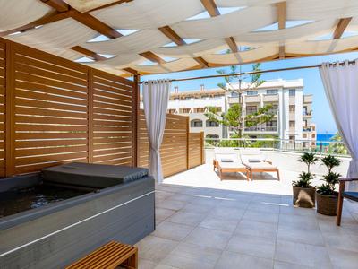 Terraza cubierta con jacuzzi, vista de tumbonas y edificio del hotel.