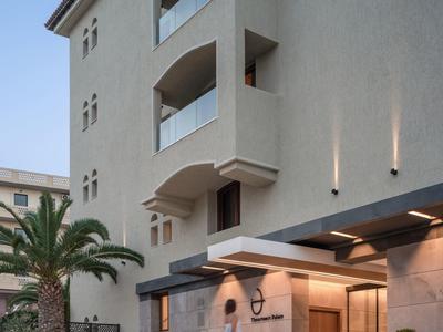 Moderner Hotelfassade mit Balkonen, Palmen und beleuchtetem Eingangsbereich bei Tagesanbruch.