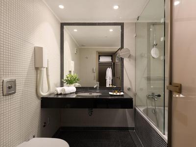 Modernes Hotelbad mit schwarzem Waschtisch, Glasdusche, Föhn und weißen Wänden.