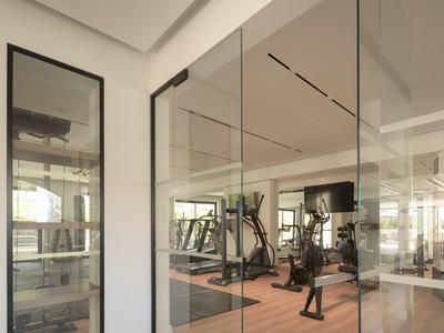 Moderner Fitnessraum mit Trainingsgeräten hinter Glaswänden, heller Raum mit Holzboden.