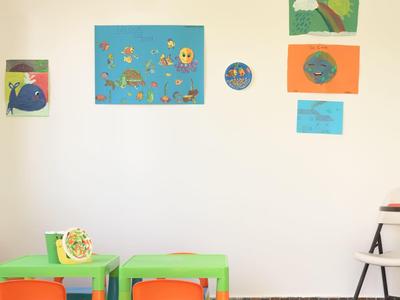 Bunter Kinderspielecke mit kleinen Tischen, Stühlen und fröhlichen Wandbildern.