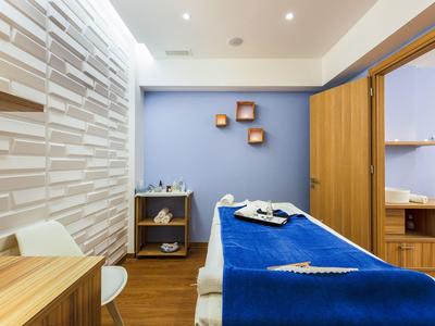 Modern eingerichteter Wellnessraum mit Massageliege, blauer Decke und holzfarbenen Möbeln.