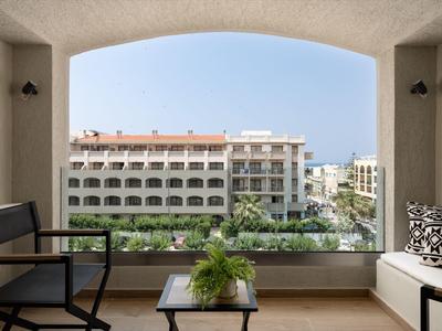 Balkon mit Sitzgelegenheiten und Blick auf modernes Hotelgebäude bei klarem Himmel.
